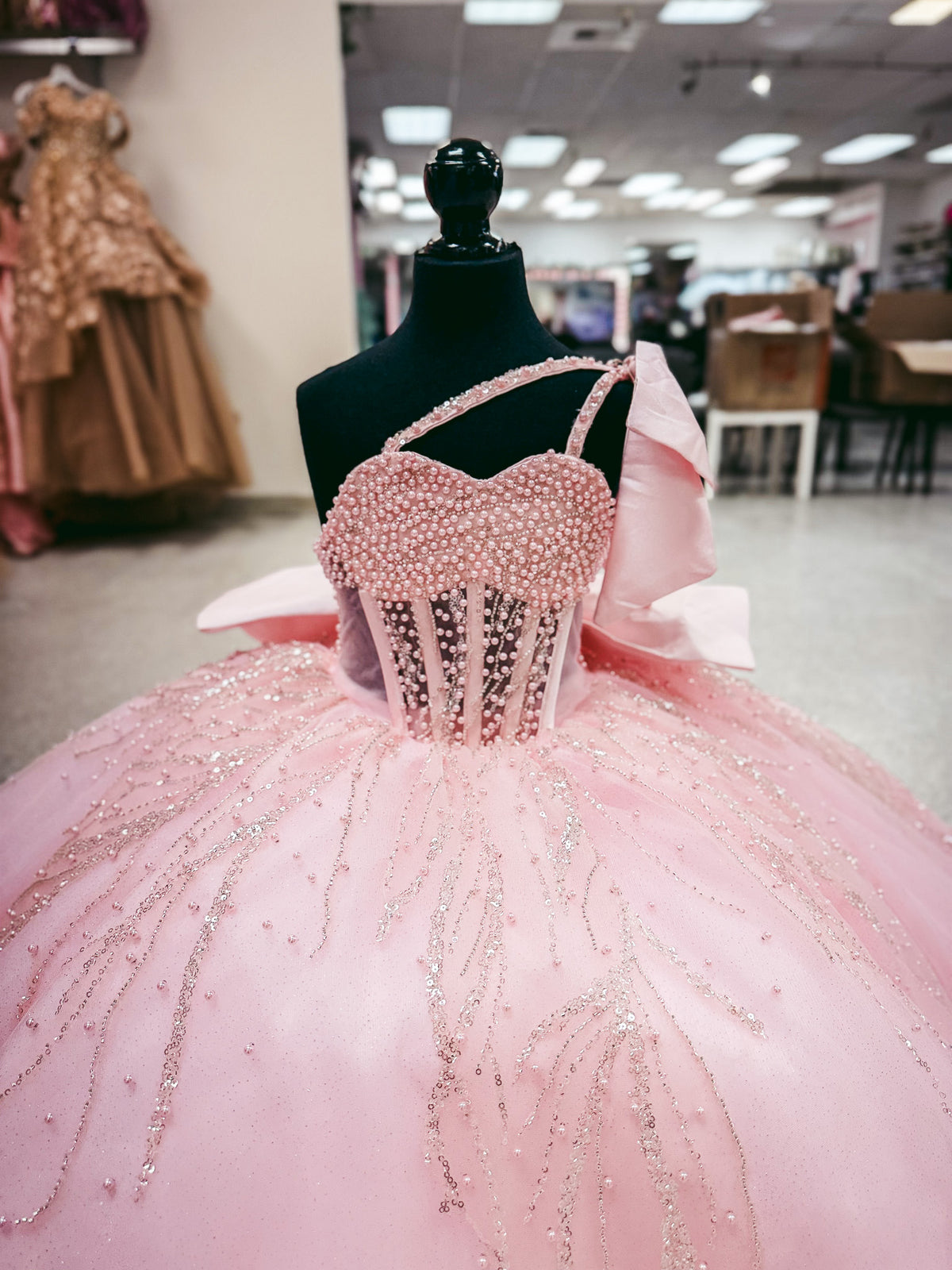 A pink ball gown with a beaded corset bodice and voluminous tulle skirt displayed on a black mannequin in a retail showroom.